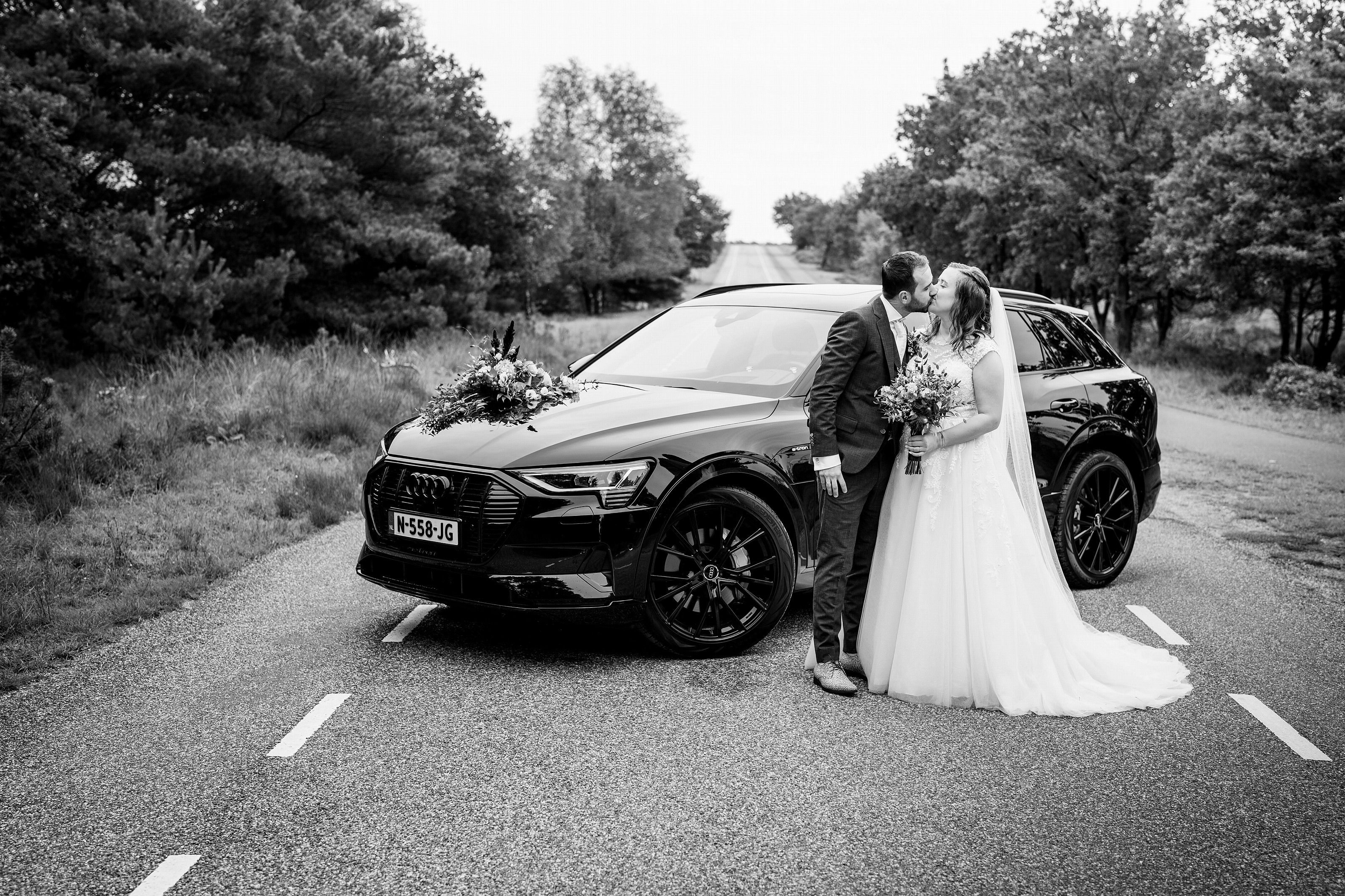 Bruidspaar kust elkaar naast de auto