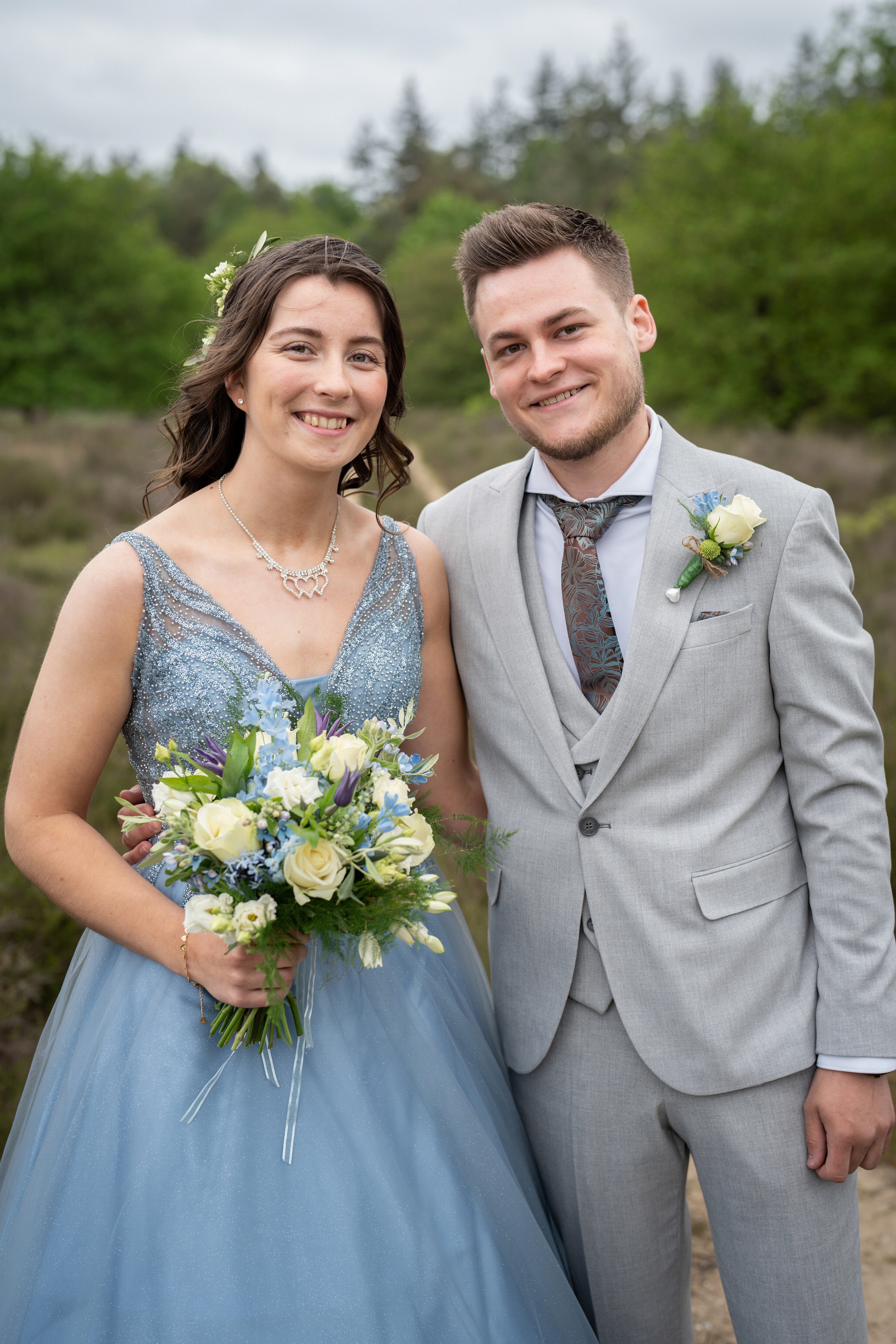 Lachend bruidspaar in het bos, bruid in een blauwe jurk met boeket