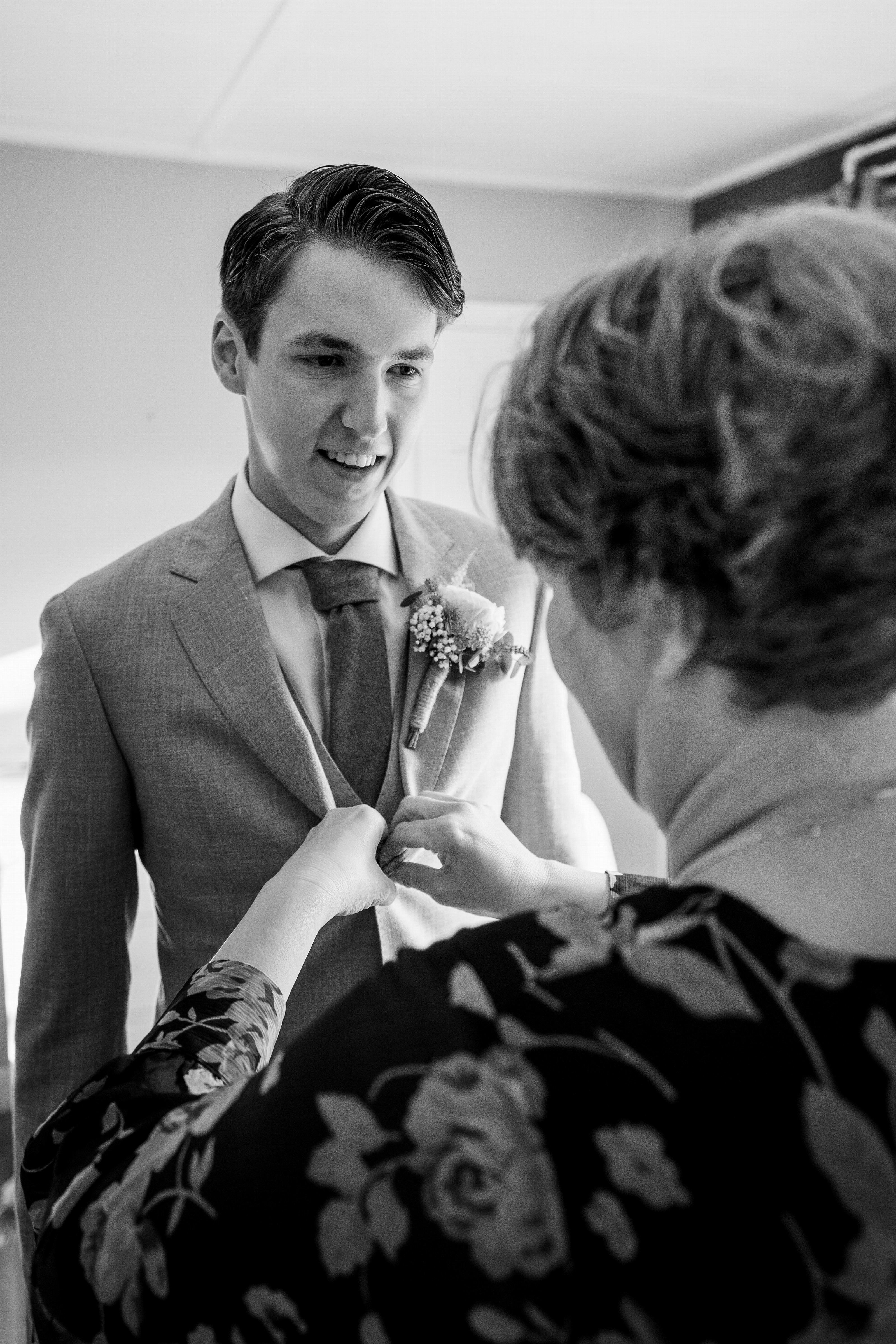Moeder speldt de corsage op bij de bruidegom, zwart-wit